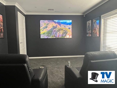 a large screen on a wall with home cinema chairs in the back of the room