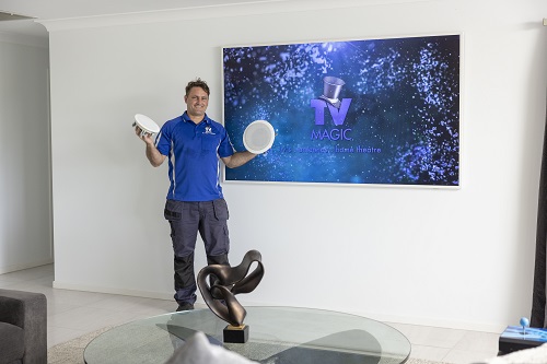 technician holding different speakers in hand, in front of a wall mounted TV