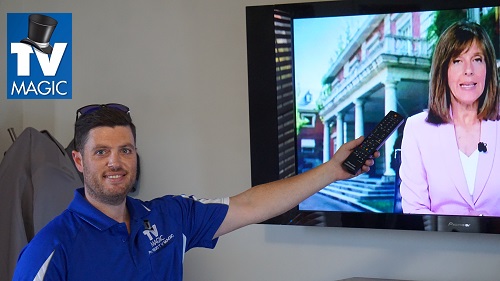 technician holding a TV remote up to a newly installed and setup TV mounted on a wall