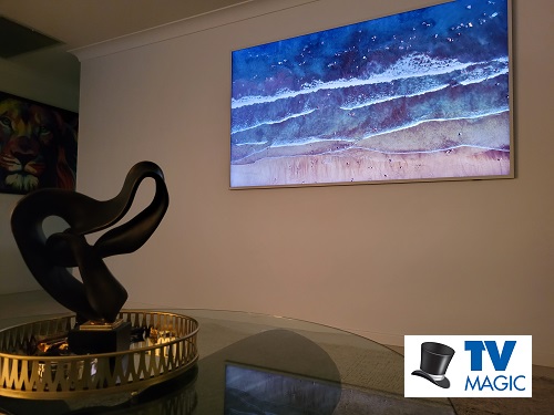 a Samsung  Frame TV mounted on a living room wall with a TV Magic logo in bottom right corner