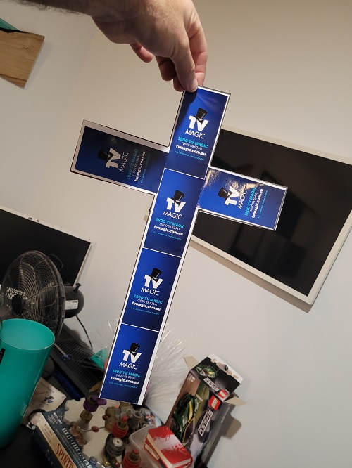 Technician holding a cross made out of TV Magic stickers, in front of a TV setup