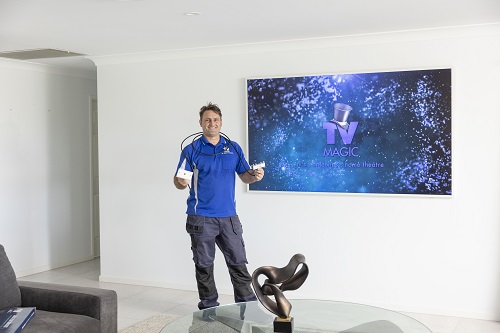 Technician holding a TV point, in front of a large TV with logo on screen