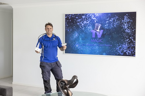 Technician holding a TV point ready for installation, in front of a large TV. Logo on screen.