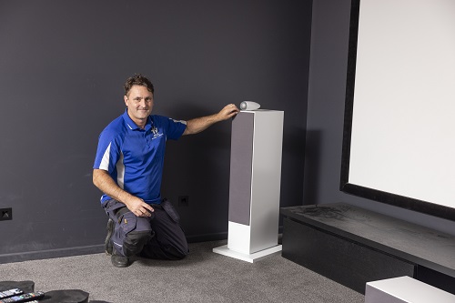 Technician kneeling next to a large speaker, in a home cinema he designed