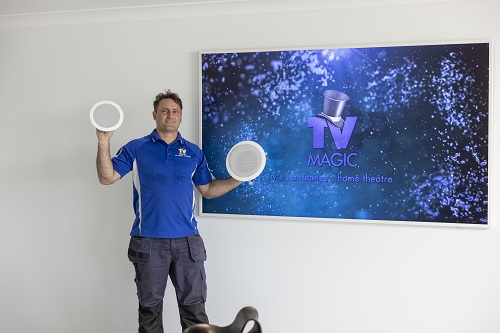 Technician holding up speakers in front of a large wall mounted TV