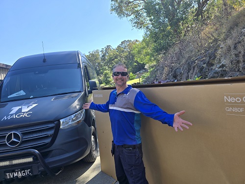Technician standing in front of a large TV, ready for delivery