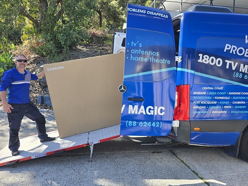 Technician loading a large TV into TV Magic van