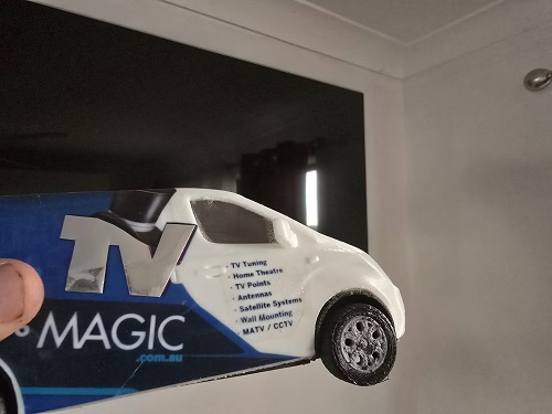 Close up of a wall mounted TV with a TV Magic mini van in front of it.