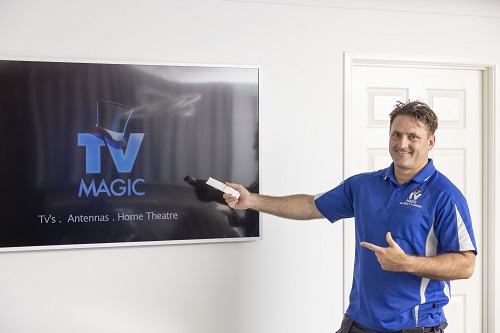 Technician holding a remote, standing next to a wall mounted TV