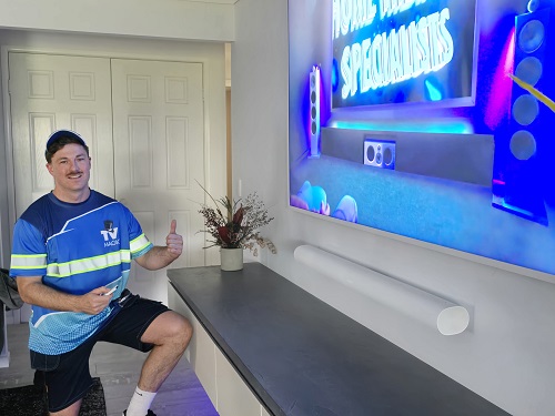 Technician next to a wall mounted TV he completed