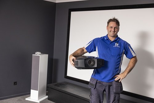 Technician holding a projector in a home theatre, ready for installation.