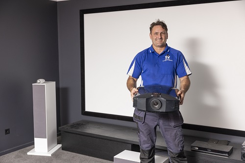Technician standing in front of a projector screen with a projector in hand