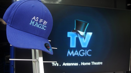 A large TV with an antenna in front of it. TV Magic cap on top of antenna which says "As If By Magic"