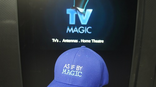 Big TV with TV Magic logo on screen. TV Magic cap in front.