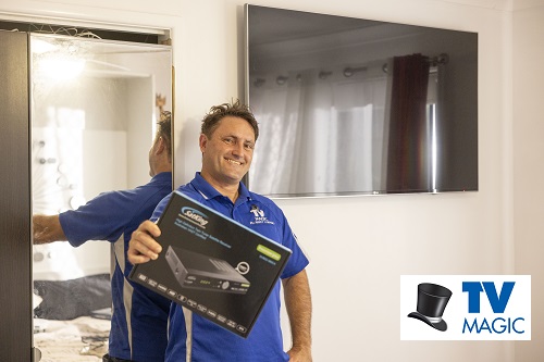 Technician holding up a vast box, in front of a wall mounted TV