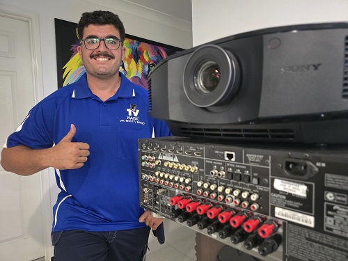 Technician standing next to projector equipment giving the thumbs up.