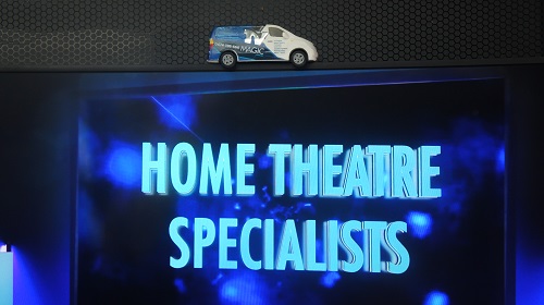 Large screen with the caption "Home Theatre Installers" on screen. Mini TV Magic van on top of it.