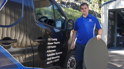 Technician with a satellite dish, standing next to his TV Magic van
