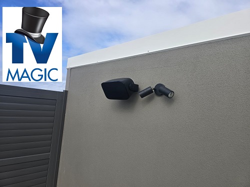 An outdoor speaker wall mounted on a concrete wall with TV Magic logo in top left corner