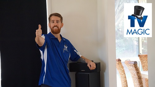 Technician with surround sound speakers he installed. TV Magic logo in top right corner