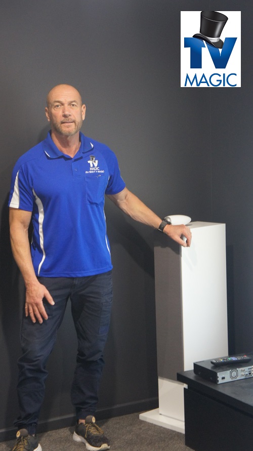 Technician standing next to a TV Magic installed surround sound system. TV Magic logo in top right corner