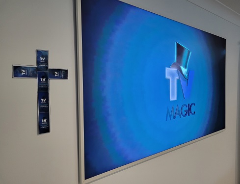 Large flat screen TV with TV Magic logo on screen. Cross next to screen made from TV Magic stickers