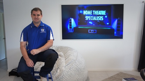 Technician sitting in front of a large TV he wall mounted.