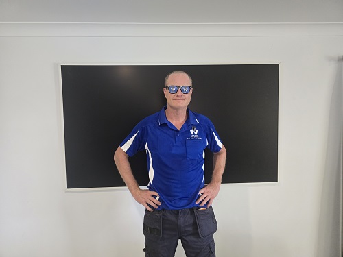 Technician standing in front of a TV he wall mounted - wearing TV Magic sunglasses.