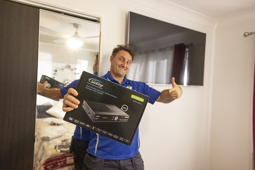 Technician holding up a vast box, in front of a wall mounted TV