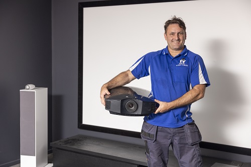 Technician holding a projector, standing in front of a projector screen