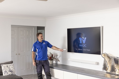 Technician next to a wall mounted TV with floating soundbar. TV Magic logo on screen.