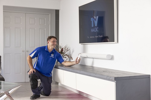 Technician next to a wall mounted TV with floating soundbar he installed.