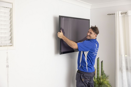 Technician holding a TV up to a wall, ready for installation