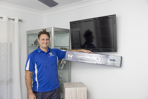 Technician with a TV he wall mounted. Also holding up a TV Magic wall bracket