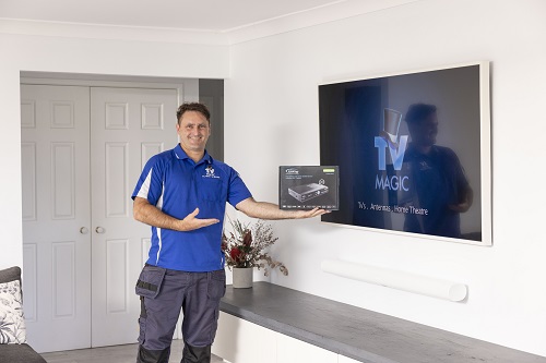 Technician holding a vast TV box in front of a wall mounted TV.