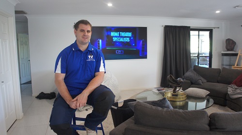 Technician sitting in front of a TV he wall mounted.