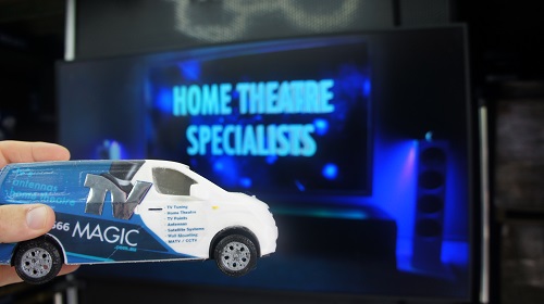 A large screen saying "Home Theatre Specialists" Mini TV Magic van in front