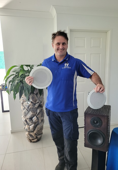 Technician holding up two speakers, standing next to a speaker tower.