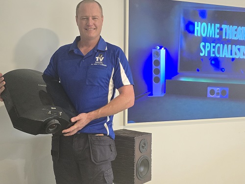 Technician holding a projector, standing next to a speaker and TV.