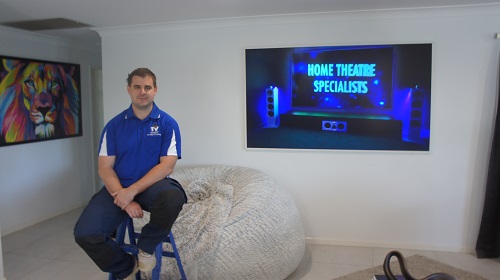 Technician sitting in front of a TV he installed and setup