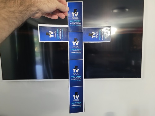 Technician holding up a cross made from TV Magic stickers, in front of a wall mounted TV