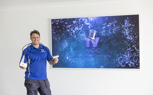 Technician standing next to a large screen with TV Magic logo on it - holding a TV point ready for installation.