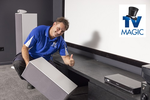 Technician in a home cinema he built. Holding a speaker. TV Magic logo in top right corner