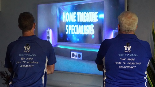 Technicians facing a large screen with caption "Home Theatre Specialists"