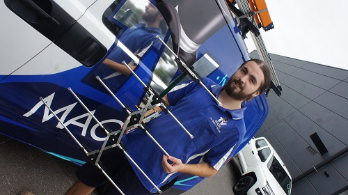 Technician next to his van with an antenna in his hand.