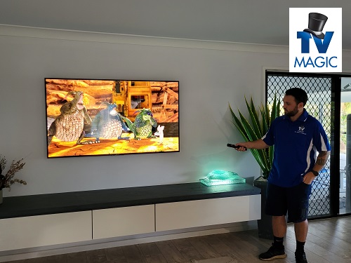 a technician setting up a new TV in a living room. TV Magic logo in bottom right corner