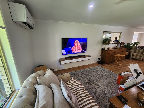 a spacious living room with a wall mounted TV and sound bar, over a floating cabinet