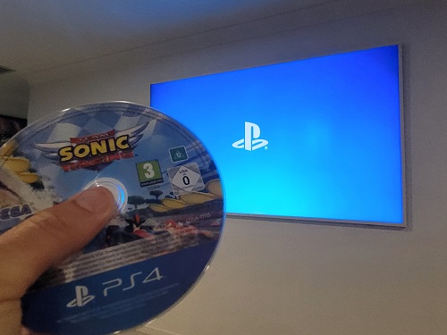 Big TV with PlayStation logo on screen, along with a gaming disc for PlayStation being held by a technician