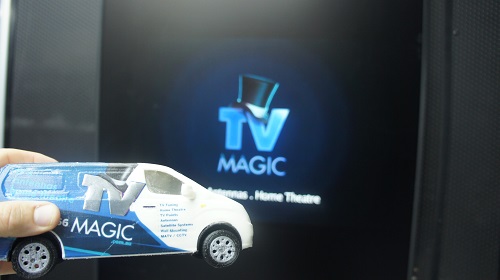 A large TV with TV Magic logo on screen and a mini TV Magic van in front of it.