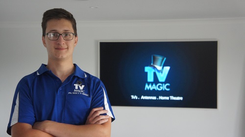 Keith in front of a wall mounted TV, with a TV Magic logo on the screen